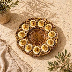 May include: A ceramic deviled egg serving platter with a brown and gold glaze. The platter has a scalloped edge and holds 12 deviled eggs, each topped with a yellow filling and a sprinkle of herbs. A decorative piece for entertaining.