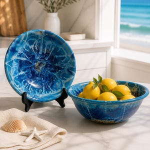 May include: Two blue decorative bowls with a marbled design. One bowl is displayed on a black stand. The other bowl is filled with yellow lemons. A seashell and starfish rest on a folded beige towel.