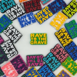 May include: A collection of rectangular plastic charms featuring the text RAVE TO THE GRAVE with a small skull icon replacing the letter O. The charms are produced in various solid colors including yellow, green, blue, pink, black, and white.
