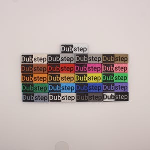 Puede incluir: Un conjunto de 20 bloques coloridos con la palabra "Dubstep" impresa en cada bloque. Los bloques están dispuestos en cuatro filas de cinco bloques cada una. Los bloques son de varios colores, incluyendo rojo, azul, verde, amarillo, naranja, morado, rosa, marrón, gris y blanco.