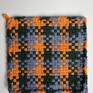May include: A woven pot holder with a geometric pattern in shades of orange, green, and gray.