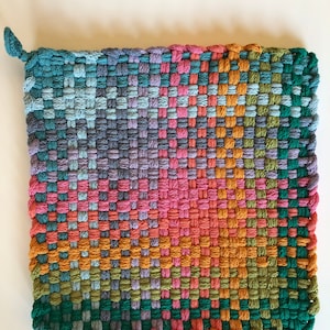 May include: A square, woven potholder in a variety of colors, including teal, pink, orange, and green. The potholder has a loop for hanging and is made of a tightly woven material. The design is a grid pattern.