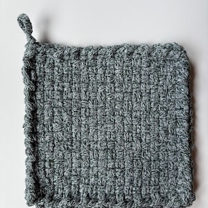 Peut inclure: Un dessous-de-plat carré tissé à la main dans des tons de gris et de blanc. Le dessous-de-plat est doté d'un coin en boucle pour l'accrocher et d'un motif texturé en tissage de panier. Les bords sont finis avec une bordure épaisse et tressée.