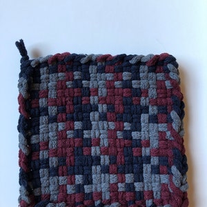 May include: A square woven pot holder with a checkered pattern in shades of grey, dark blue, and burgundy.