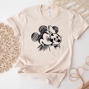 May include: A beige t-shirt with a black and white sketch of Mickey Mouse and Minnie Mouse.