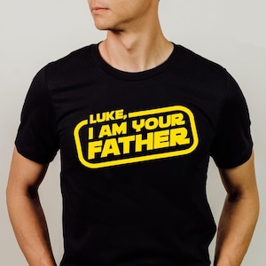 May include: A black t-shirt with a yellow graphic that says "LUKE, I AM YOUR FATHER" in a Star Wars-inspired font.