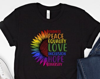Könnte beinhalten: Schwarzes T-Shirt mit einem Regenbogen-Sonnenblumen-Motiv und den Worten "Kindness, Peace, Equality, Love, Inclusion, Hope, Diversity". Das Shirt wird mit weißen Sneakern und einer blauen Jeans kombiniert.