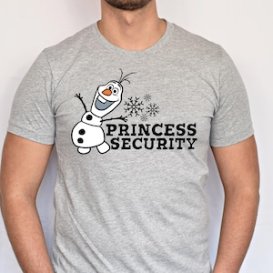 以下が含まれることがあります： オラフ雪だるまの漫画のイメージと「PRINCESS SECURITY」の文字が黒でプリントされた、明るい灰色のTシャツ。デザインには雪の結晶が含まれています。