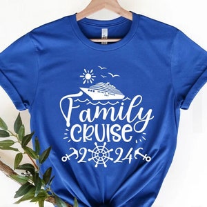 Puede incluir: Una camiseta azul real con un gráfico blanco de un crucero, sol y gaviotas. El texto "Family Cruise 24/7" también está impreso en la camiseta.