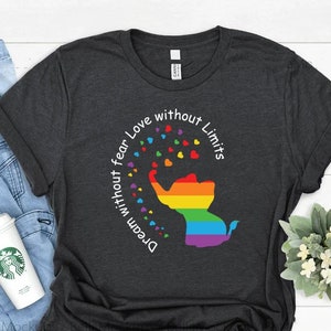Könnte beinhalten: Ein dunkelgraues T-Shirt mit einem Regenbogen-Elefanten-Motiv und dem Text "Dream without fear Love without limits".
