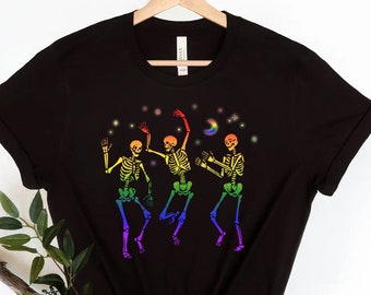 Könnte beinhalten: Schwarzes T-Shirt mit einem Motiv von drei regenbogenfarbenen Skeletten, die unter einem Halbmond und Sternen tanzen.