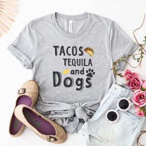 May include: Gray t-shirt with the text "Tacos Tequila and Dogs" in black lettering. The shirt has a yellow lemon slice and a paw print graphic.
