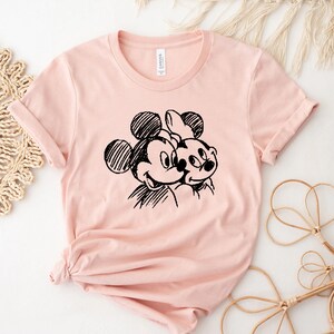 May include: A pink t-shirt with a black and white sketch of Mickey Mouse and Minnie Mouse.