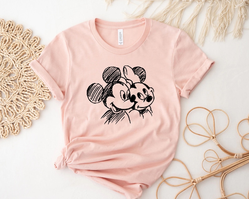 May include: A pink t-shirt with a black and white sketch of Mickey Mouse and Minnie Mouse.