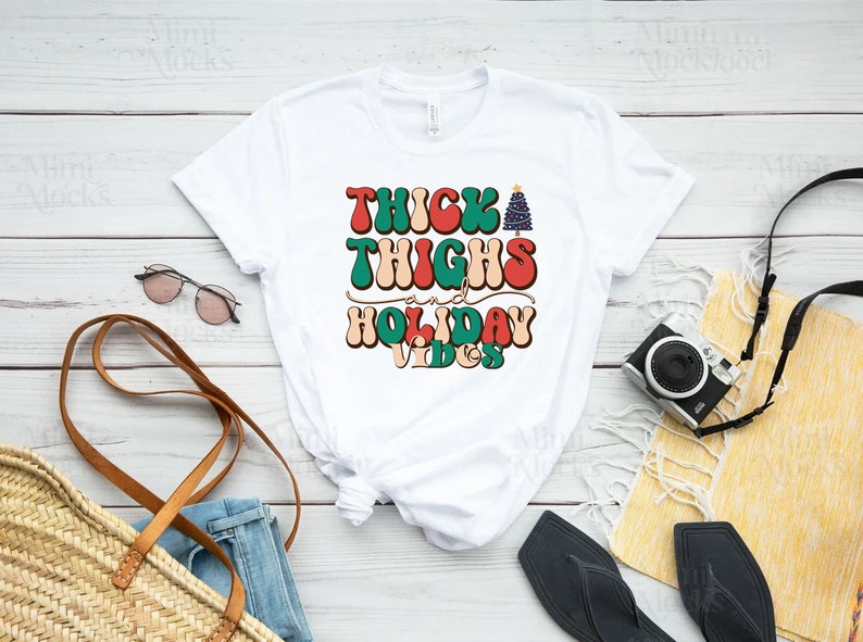 Puede incluir: Camiseta blanca con un gr&aacute;fico de estilo retro que dice "Thick Thighs and Holiday Vibes" con un gr&aacute;fico de &aacute;rbol de Navidad.