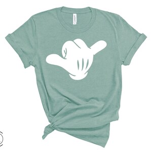 May include: A teal blue t-shirt with a white hand making the shaka sign.