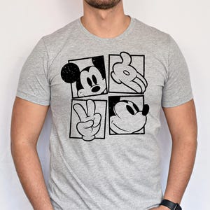 May include: A gray t-shirt featuring a black and white graphic of Mickey Mouse. The design is divided into four squares, each showcasing a different element of Mickey's iconic features: his face, hand, and peace sign.