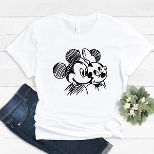 May include: White t-shirt with a black and white sketch of Mickey Mouse and Minnie Mouse.