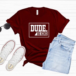 May include: A maroon t-shirt with white text that reads "DUDE. BE KIND" in a rectangular box.