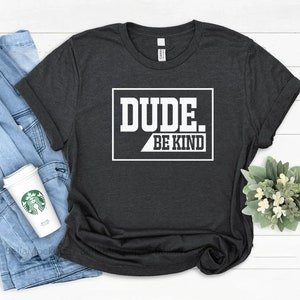 May include: A dark gray t-shirt with a white graphic that says "DUDE. BE KIND" in a white box with a black outline.