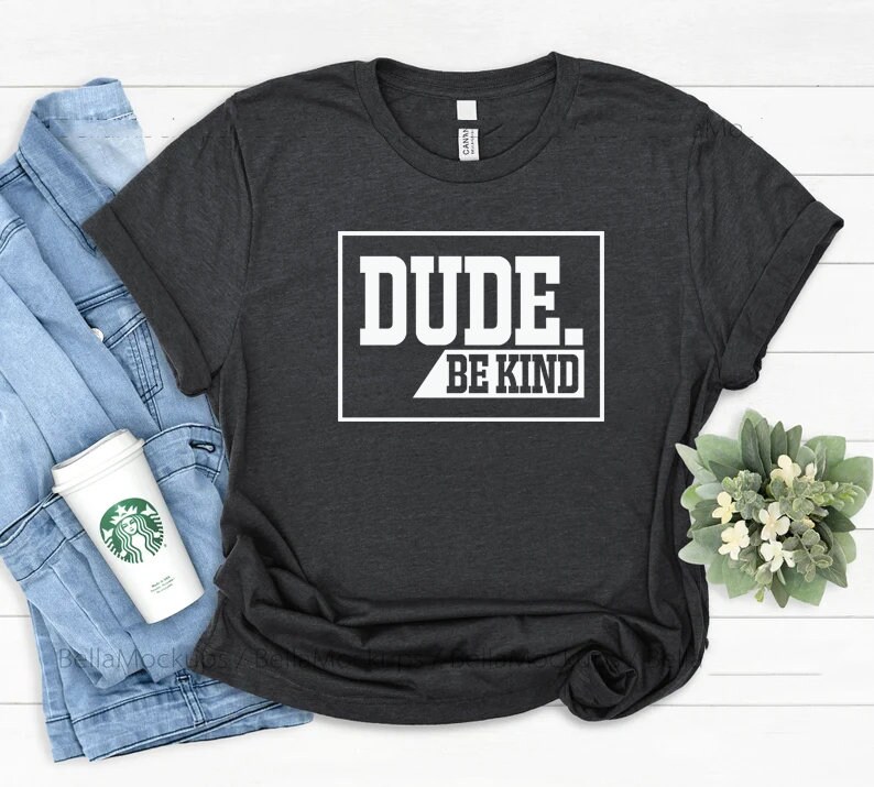 May include: A dark gray t-shirt with a white graphic that says "DUDE. BE KIND" in a white box with a black outline.