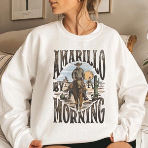 May include: White sweatshirt with a vintage graphic design featuring a cowboy riding a horse with the text "Amarillo by Morning".