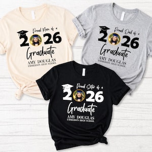 May include: Three t-shirts with graduation-themed designs. One is cream-colored, one is gray, and one is black. Each shirt features the text "Proud Mom of a 2026 Graduate", "Proud Dad of a 2026 Graduate", and "Proud Sister of a 2026 Graduate".