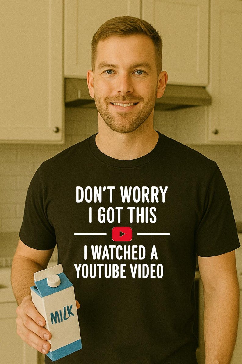 Pode incluir: Uma camiseta preta com o texto "Don't worry I got this I watched a YouTube video" e um &iacute;cone de reprodu&ccedil;&atilde;o vermelho. A pessoa est&aacute; segurando uma caixa de leite azul e branca.