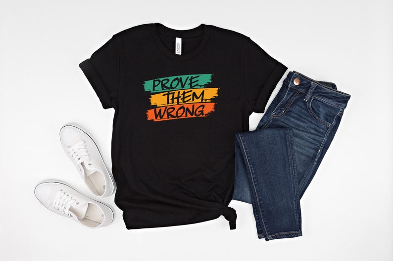 May include: Black t-shirt with the text "PROVE THEM WRONG" in green, orange, and yellow paint strokes.