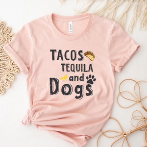 May include: A pink t-shirt with the text "Tacos Tequila and Dogs" in black lettering. A yellow lemon and a black paw print are included in the design.