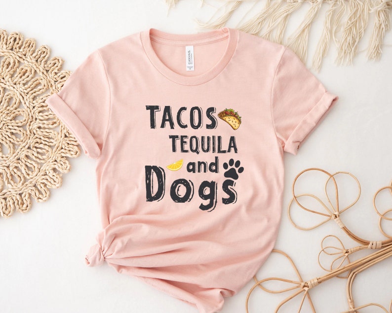 May include: A pink t-shirt with the text "Tacos Tequila and Dogs" in black lettering. A yellow lemon and a black paw print are included in the design.