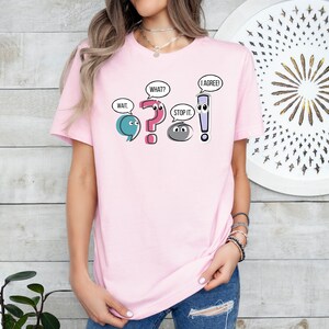 May include: A pink t-shirt with a graphic of punctuation marks with faces. The punctuation marks are a semicolon, question mark, period, and exclamation point. The text on the shirt reads "Wait," "What?" "Stop it." and "I agree!"