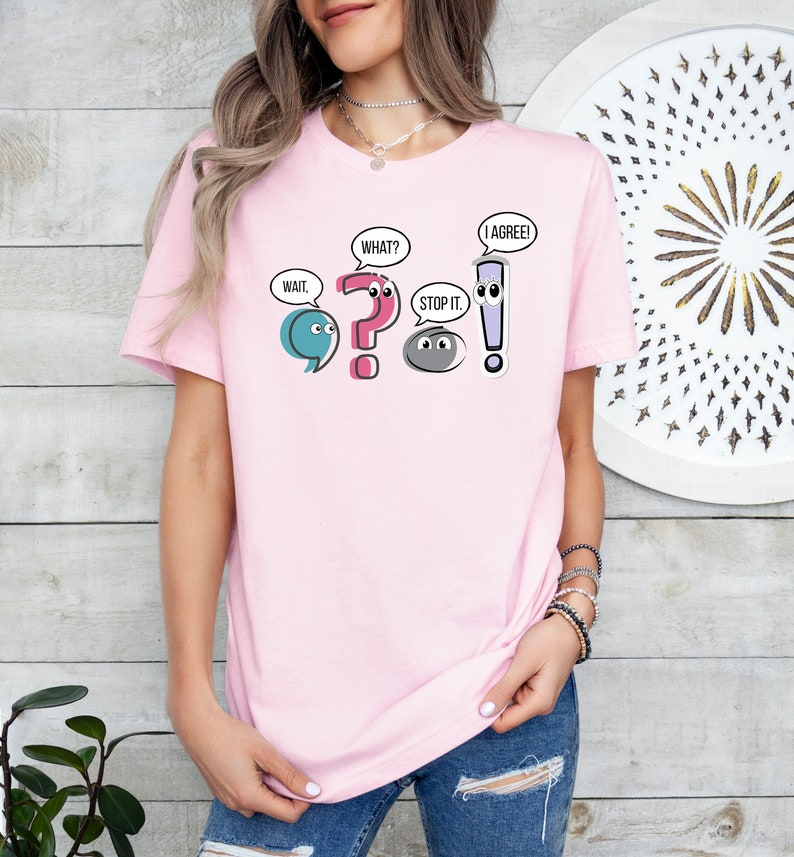 May include: A pink t-shirt with a graphic of punctuation marks with faces. The punctuation marks are a semicolon, question mark, period, and exclamation point. The text on the shirt reads "Wait," "What?" "Stop it." and "I agree!"