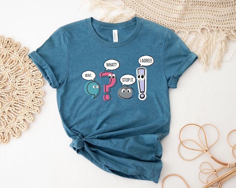 May include: Teal blue t-shirt with a graphic of punctuation marks with eyes and speech bubbles. The speech bubbles say "Wait", "What?", "Stop it", and "I agree!"