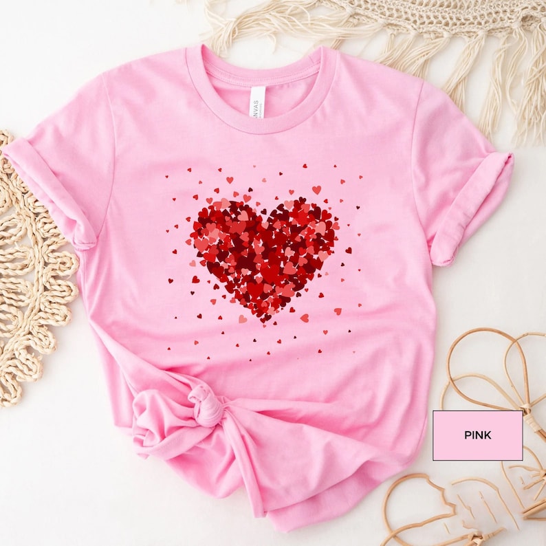 May include: Pink t-shirt with a red heart made of smaller hearts. The heart is surrounded by smaller red hearts.