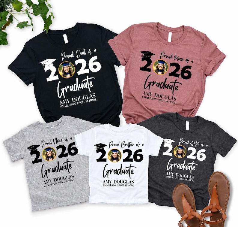 May include: Assorted t-shirts with graduation-themed designs. The shirts are black, pink, gray, white, and dark gray. Each shirt features the text "Proud Dad of a 2026 Graduate", "Proud Mom of a 2026 Graduate", "Proud Niece of a 2026 Graduate", "Proud Brother of a 2026 Graduate", and "Proud Sister of a 2026 Graduate".