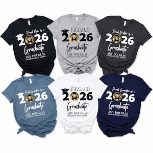 May include: A collection of graduation-themed t-shirts in various colors, including black, gray, and blue. Each shirt features the text "Proud Mom/Brother/Grandpa of a 2026 Graduate" with a photo and the graduate's name and school.