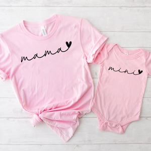 May include: Pink t-shirt with the word "mama" in black script with a small black heart. A pink baby onesie with the word "mini" in black script with a small black heart.