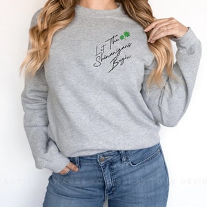 Peut inclure: Un sweat-shirt gris avec le texte "Let the Shenanigans Begin" en &eacute;criture noire avec des tr&egrave;fles verts.