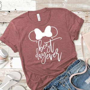 May include: A maroon t-shirt with a white bow and the text "best day ever" in white cursive writing.