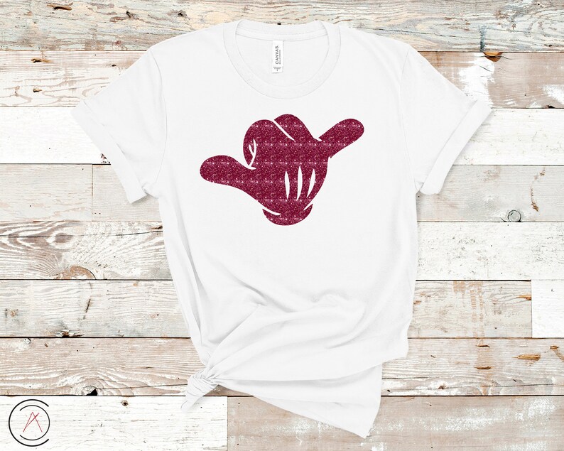 May include: White t-shirt with a burgundy glitter hand making the shaka sign.