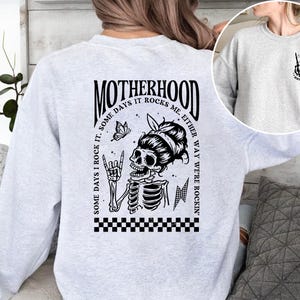 May include: Gray sweatshirt with a black and white graphic of a skeleton with a butterfly and the text "Motherhood. Some days I rock it. Some days it rocks me. Either way we're rockin'."