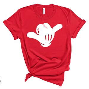 May include: Red t-shirt with a white hand making a shaka sign.