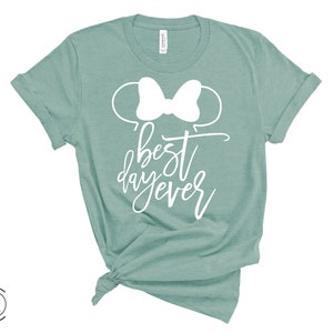 May include: A teal green t-shirt with a white bow and the text "best day ever" printed on the front.