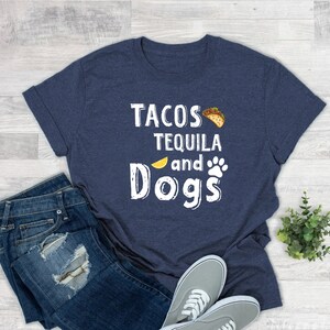 May include: A navy blue t-shirt with white text that reads "Tacos Tequila and Dogs". The text is surrounded by a lemon slice, a paw print, and a taco.