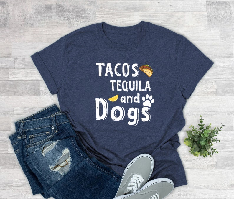 May include: A navy blue t-shirt with white text that reads "Tacos Tequila and Dogs". The text is surrounded by a lemon slice, a paw print, and a taco.