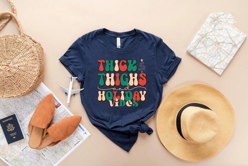 Puede incluir: Camiseta azul marino con un gr&aacute;fico de estilo retro que dice "Thick Thighs and Holiday Vibes". El gr&aacute;fico presenta colores rojo, verde y blanco.