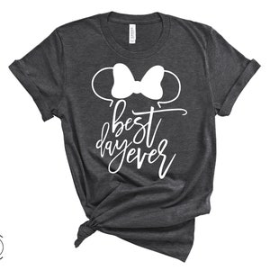 May include: A dark gray t-shirt with a white outline of Mickey Mouse ears and a bow. The text "best day ever" is written in white cursive lettering.