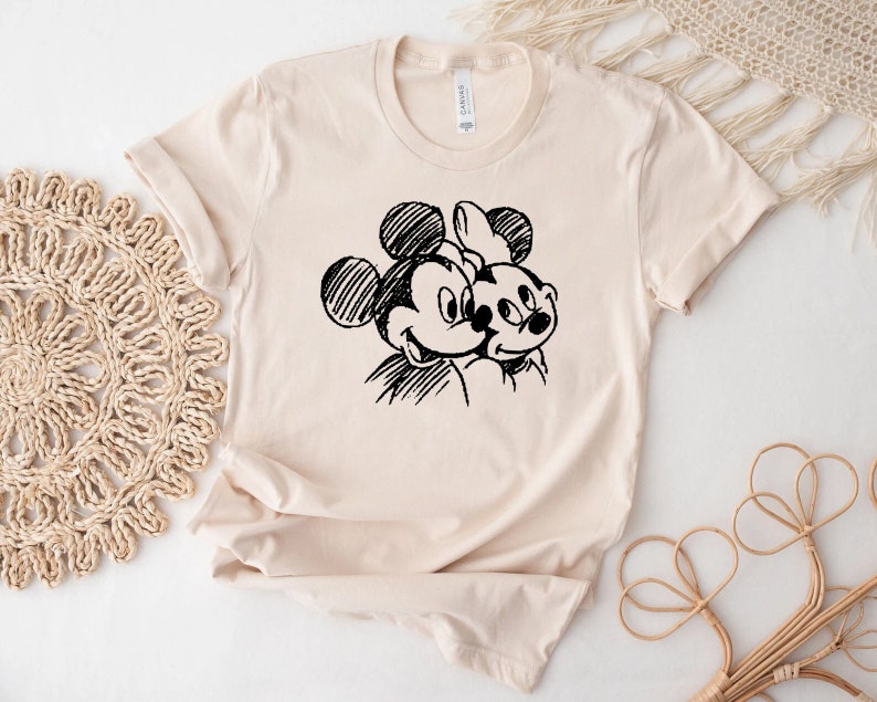 May include: A beige t-shirt with a black and white sketch of Mickey Mouse and Minnie Mouse.