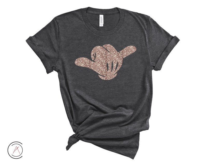 May include: A dark grey t-shirt with a rose gold glitter hand making the shaka sign.